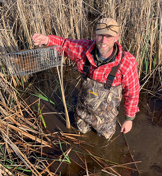 Adam Ahlers standing in water holding cage with beaver inside