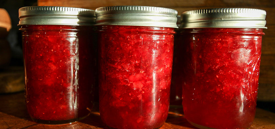 Closeup, three jars of canned red jelly sitting on a table Closeup, three jars of canned red jelly sitting on a table