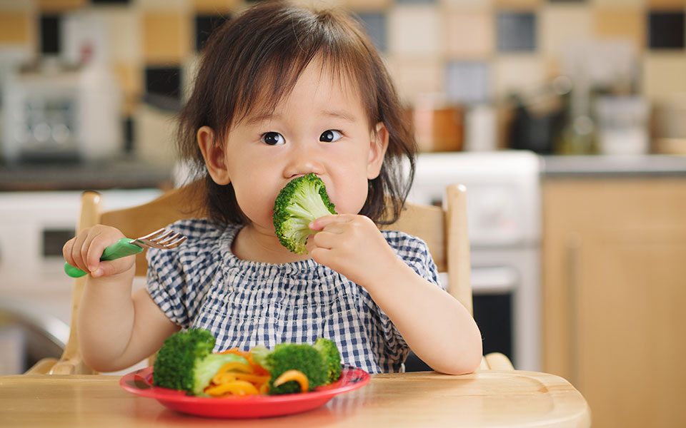 child sitting at a table eating broccoli