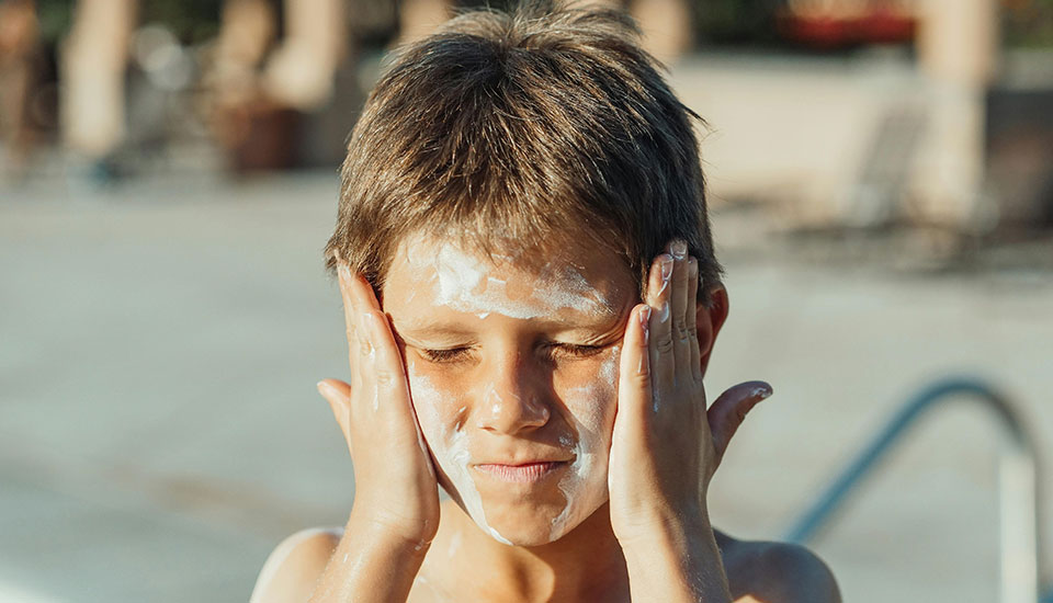 Closeup of boy at the swimming pool rubbing sunscreen on his face
