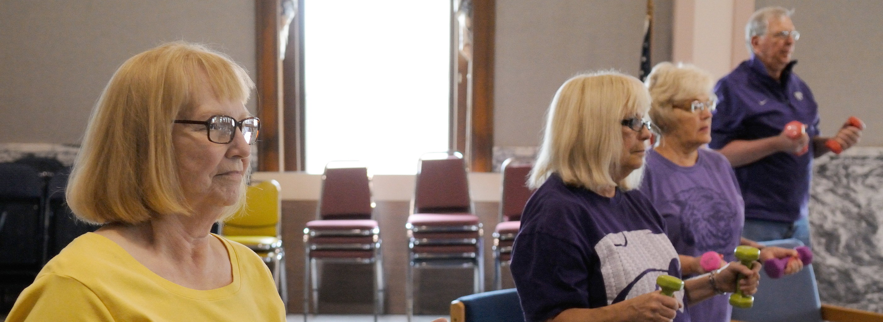 Three women and one man lifting light hand weights. 