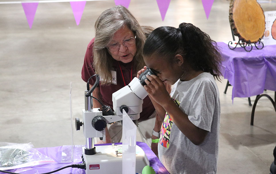 Woman assisting young girl who is looking through a miscroscope
