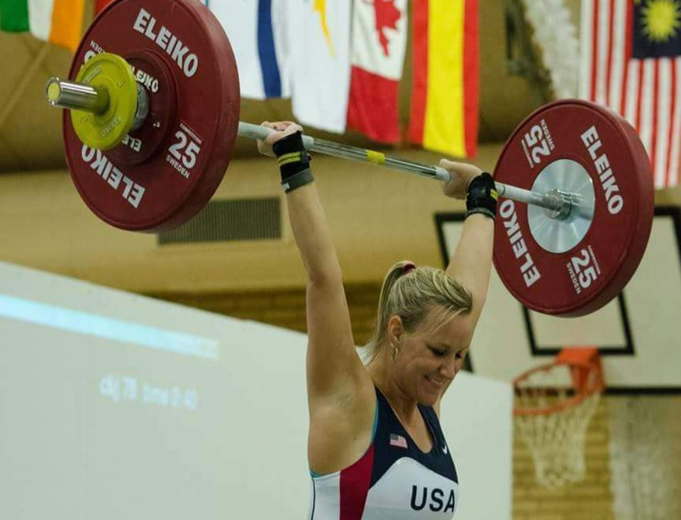 Woman wearing a jersey that reads USA and holding weight bar with heavy weights above her head Woman wearing a jersey that reads USA and holding weight bar with heavy weights above her head