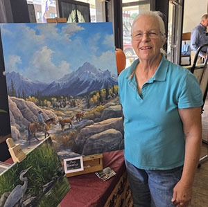 Woman wearing blue shirt and jeans standing next to painting of horses in a river canyon