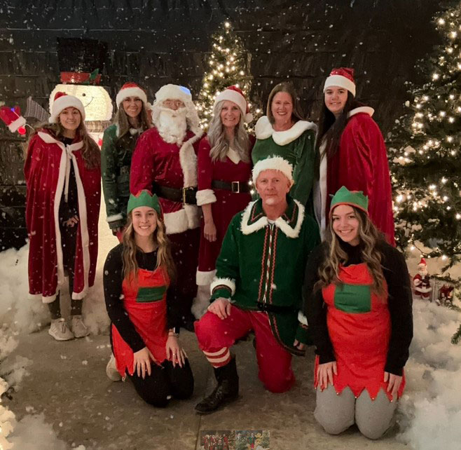 Several people dressed as Christmas elves with snow falling around them