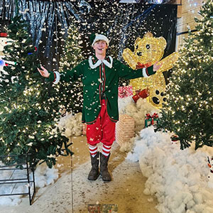 Young man dressed as a Christmas elf, smiling and catching falling snow