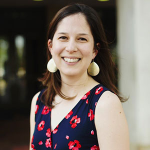 picture of woman in blue dress with red flowers standing in front a building