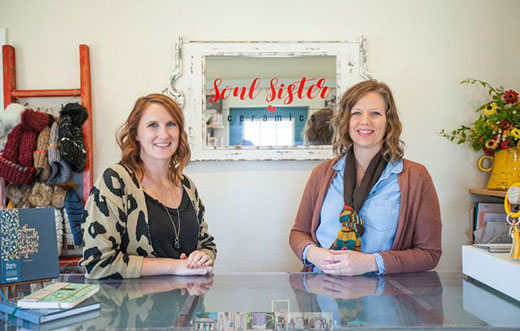 Two women sitting in front of sign, Soul Sister Ceramics