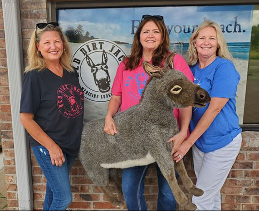 three woman standing in front of store holding stuffed animal donkey toy