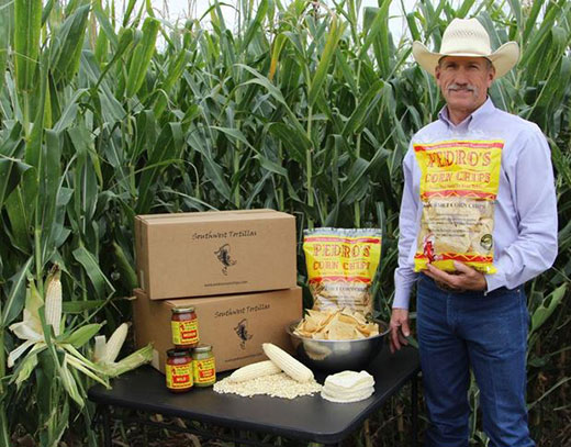 Man holding bag of tortilla chips standing in front of corn field