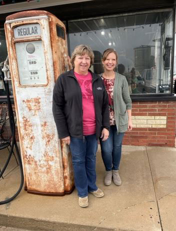 Two ladies standing next to rusted gas pump