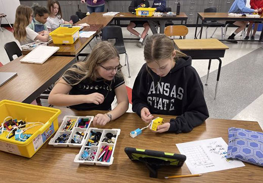 two girls sitting at table building a robotic lego