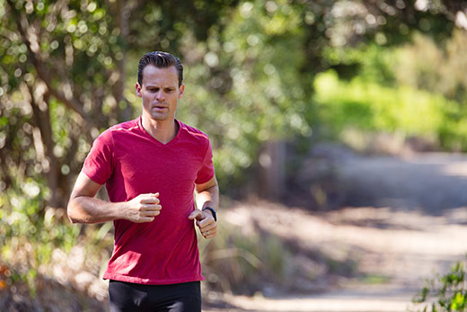 Man with red shirt running on tree-lined trail