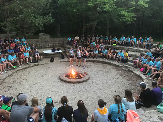 Large number of 4-H youth sitting around campfire pit