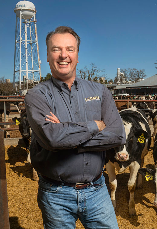 Man smiling while standing near pen of dairy cattle