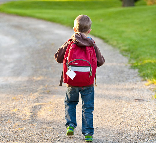 small boy walking down road with backpack