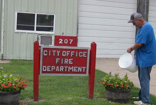 Man watering flowers in front of city fire department sign