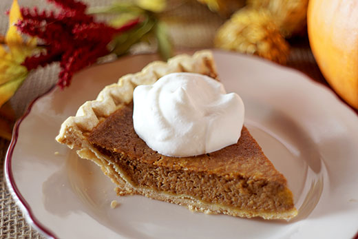 Slice of pumpkin pie with whipped cream on a white plate Slice of pumpkin pie with whipped cream on a white plate