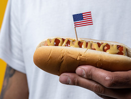 Closeup of man holding hot dog with American flag Closeup of man holding hot dog with American flag
