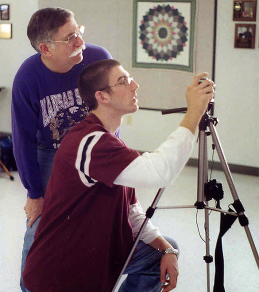 Man looking over youth's shoulder with camera and tripod