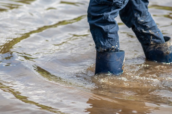 image of person from the knee down wearing rain boots standing in flood waters